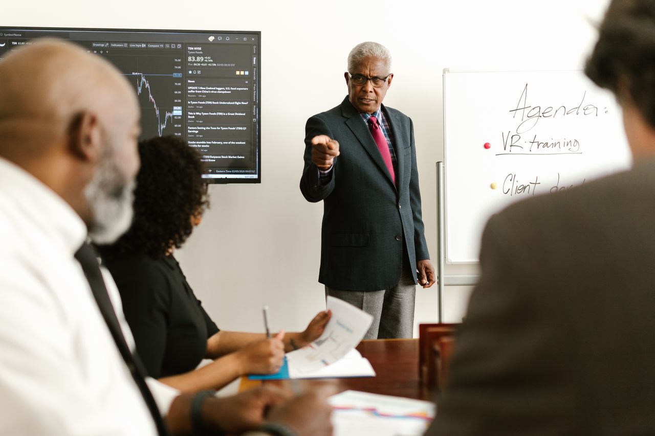 Gestion de projets Senior executive conducting a business meeting with colleagues, discussing agenda on a whiteboard.