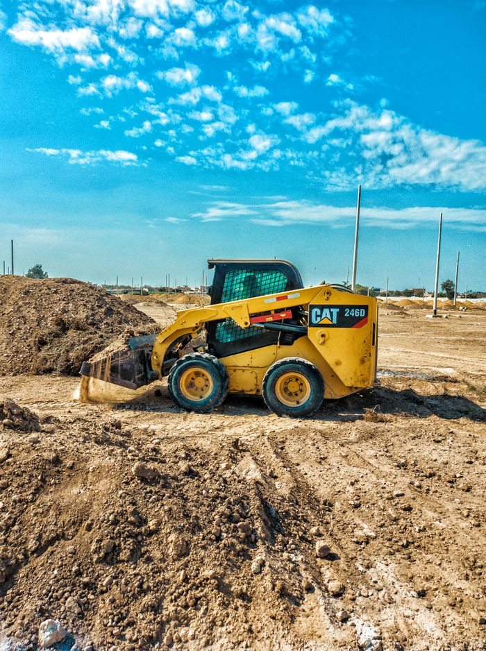 Construction & Travaux publics Skid steer loader at a daytime construction site with blue sky backdrop.